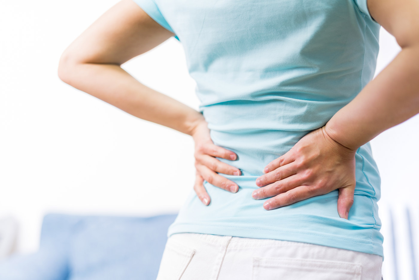 Frau hält sich die Hände an den unteren Rücken, ein typischer Fall für eine Schmerztherapie in der Orthopädie