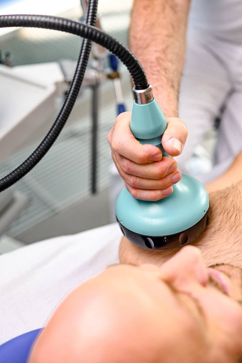 Stoßwellentherapie an der linken Schulter eines Patienten durch medizinische Fachkraft